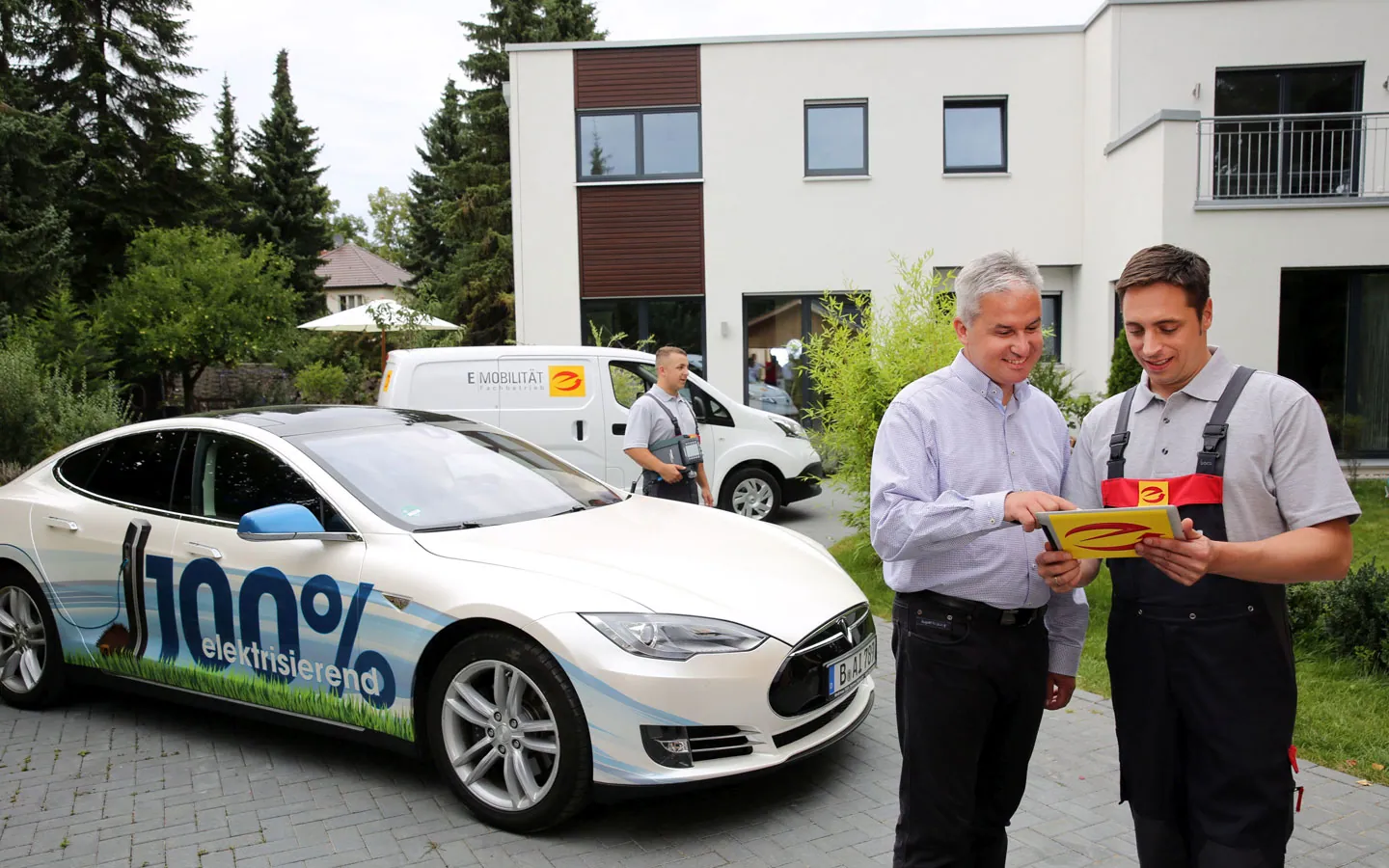 E-Mobilität - Mitarbeiter mit Kunden vor Elektrofahrzeugen 100% elektrisch · ARNOLD Elektrotechnik